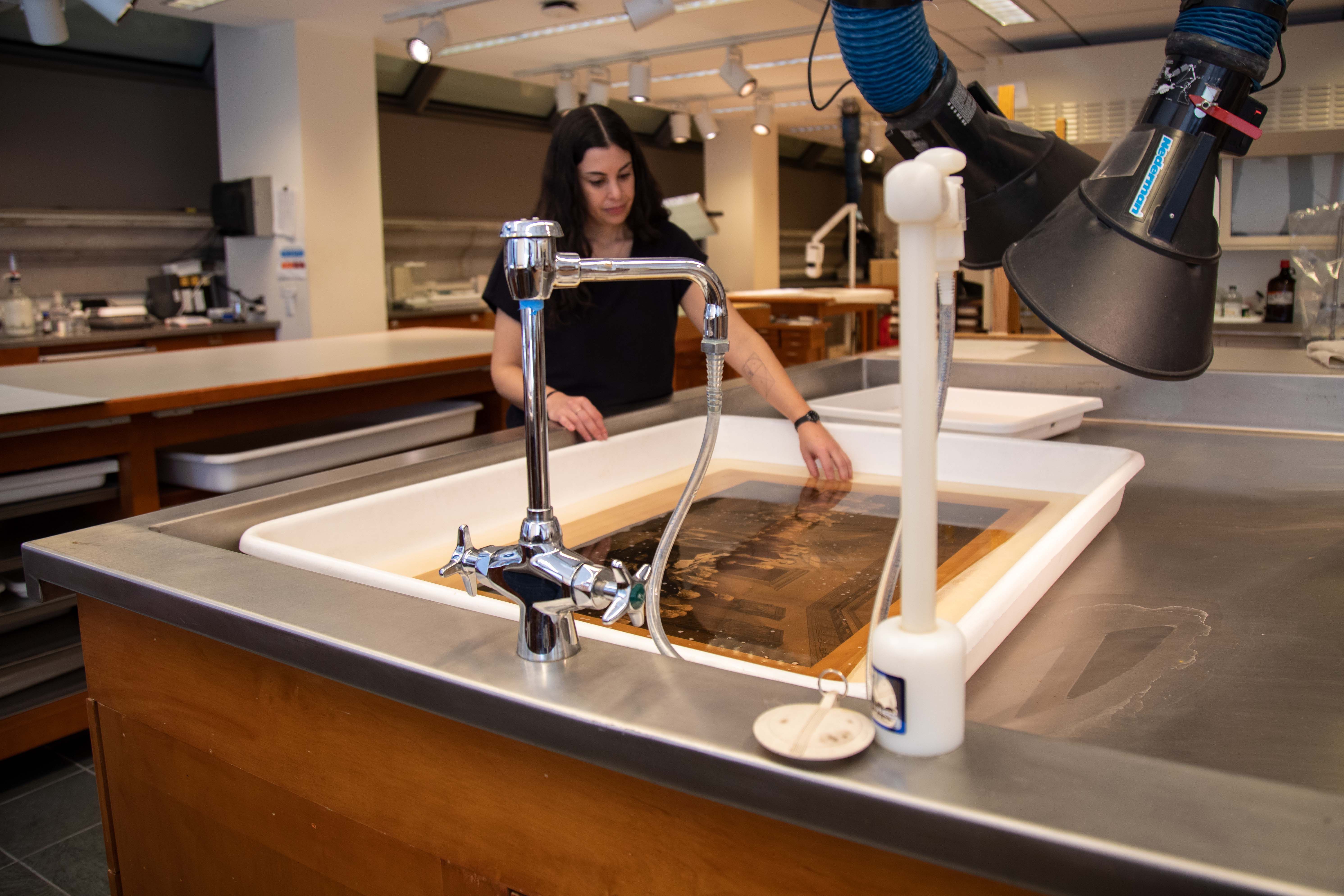 Loike in the paper conservation lab at the met. A piece of art is submerged in water in the sink in front of her.